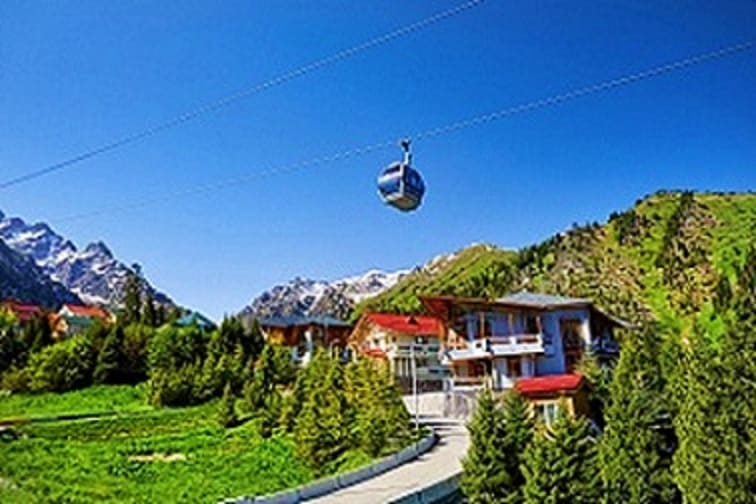 Aerial tramway cable car descending over Alpine valley with mountain lodge and snow-capped peaks in Kazakhstan